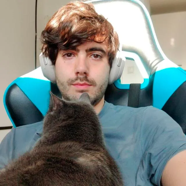 Guillermo wearing headphones with his cat Willy sitting in his lap